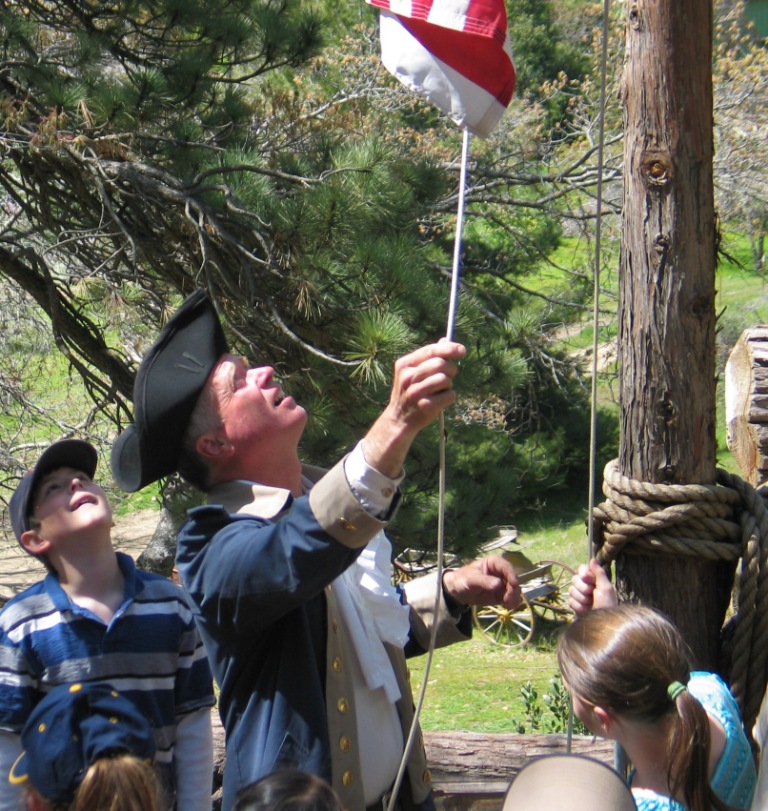 Author and Smith Ranch tour guide raising the "76" Battle of Bennington flag at log Fort Daniel Boone in Julian CA